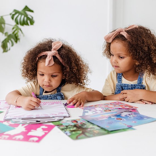 Une fille dessine dans un livre d'activités Gabby's Dollhouse à une table.