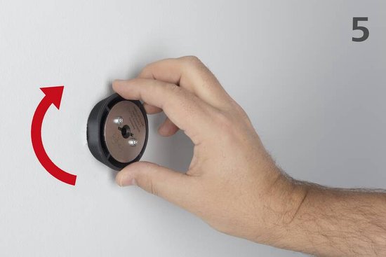 Hand monteert zwarte Wolfcraft adapter op een muur, rode pijl toont draairichting.