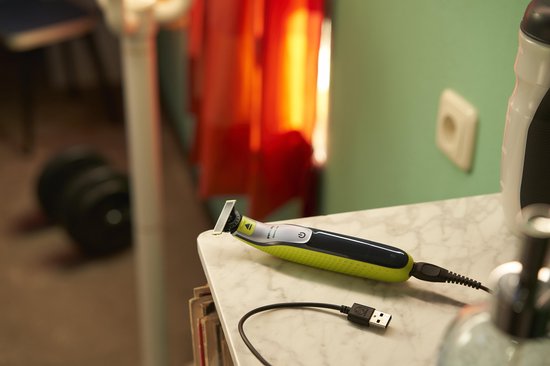 Gele en zwarte Philips OneBlade trimmer op een marmeren tafel, met een USB-kabel aangesloten.