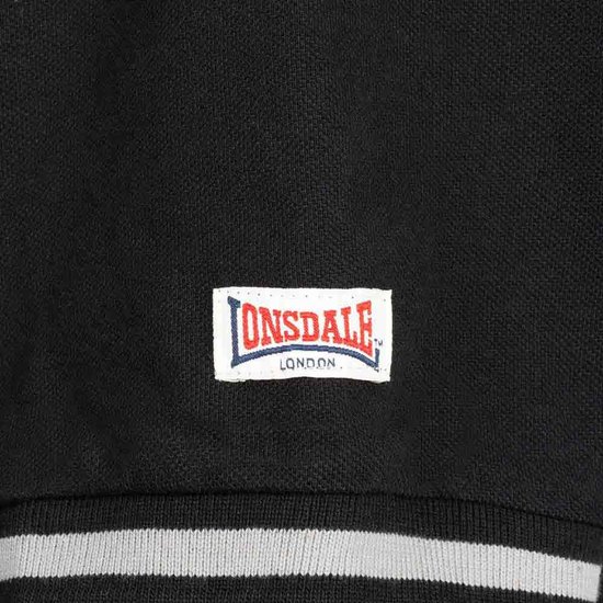 Detail van een witte badge met rood en blauw Lonsdale London logo op een zwarte Lonsdale polo.