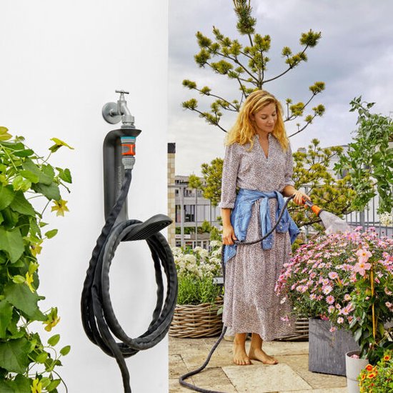 Vrouw met jurk en spijkerjasje sproeit bloemen op een balkon met Gardena Liano slang.