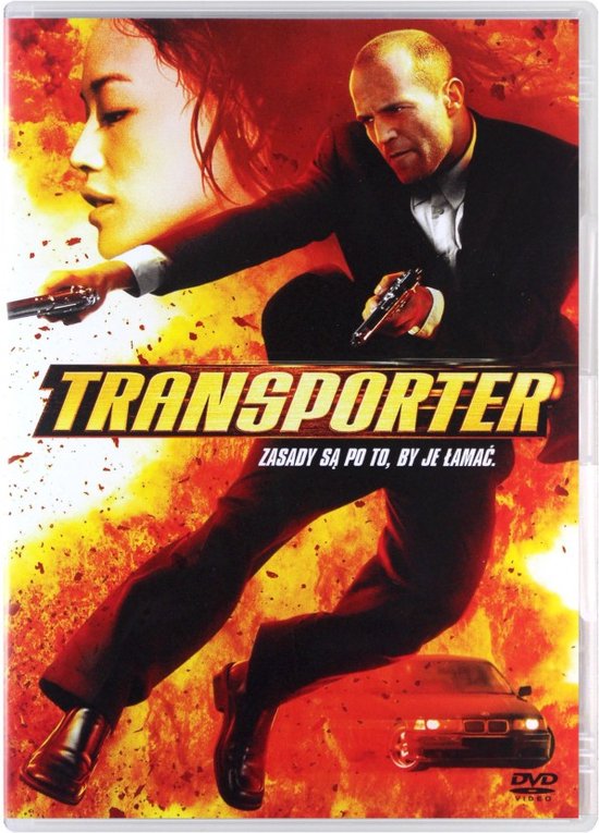 Jason Statham als de Transporter in een zwart pak met pistool, met een vrouw op de achtergrond.
