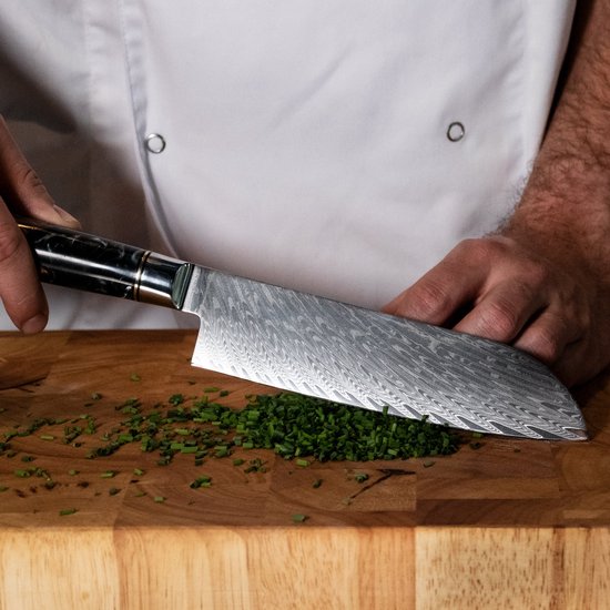 Een chef-kok snijdt bieslook met een Japans santokumes met damastpatroon en zwart/houten handvat.