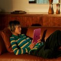 Personne allongée sur un canapé marron tenant un iPad rose.