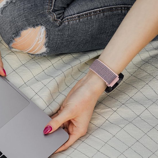 Roze nylon horlogeband om een pols, zittend persoon met laptop en gescheurde jeans.
