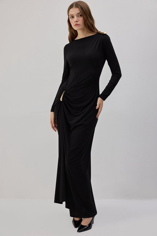 Model in zwarte maxi-jurk met lange mouwen, gouden schouderdetail en gedrapeerde heup met gouden gesp.