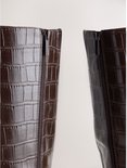 Detailopname van de zijkant van de bruine laarzen met krokodillenmotief en een rits met "NEXT"-logo.