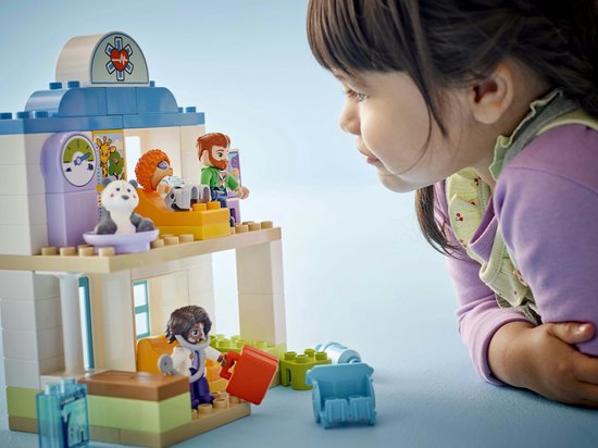 Meisje kijkt naar LEGO Duplo dokterscentrum. Met dokterskoffer, weegschaal en röntgenapparaat.