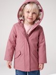 Meisje met blond haar, lachend, met roze regenjas met bloemenprint op de teddy voering van de capuchon, en spijkerbroek.