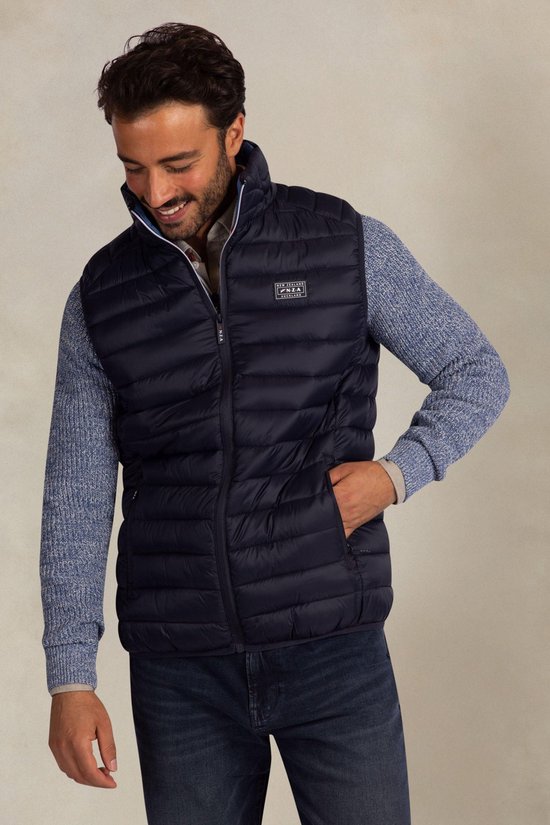 Man met donkerblauwe gewatteerde bodywarmer en Patch 'New Zealand Auckland' op de borst, gedragen over blauw vest.