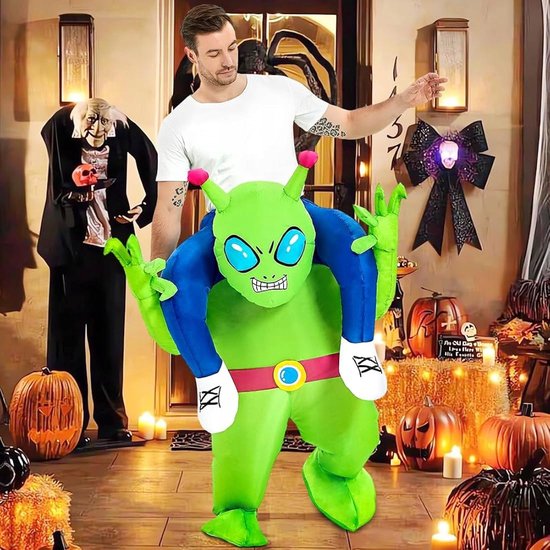 Man in een groen opblaasbaar Alien-kostuum voor een huis versierd voor Halloween met pompoenen.