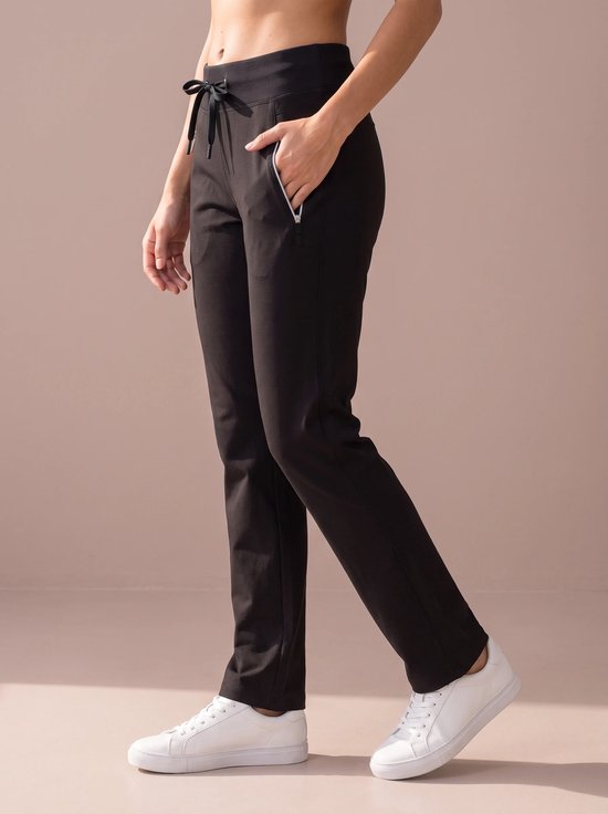 Zijaanzicht van een model in een zwarte sportbroek met ritszak en trekkoord, gecombineerd met witte sneakers.