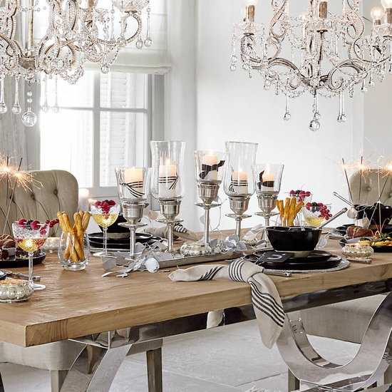 Eettafel gedekt met zilveren kandelaars met witte kaarsen, feestelijke hapjes en kristallen kroonluchters.