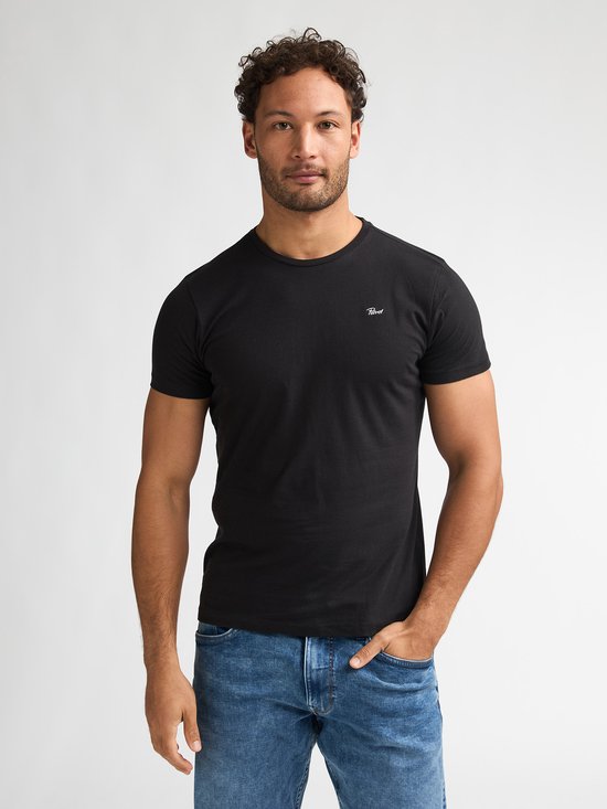 Model draagt een zwart T-shirt met ronde hals, korte mouwen en klein wit 'Petrol' logo op de borst, gecombineerd met jeans.