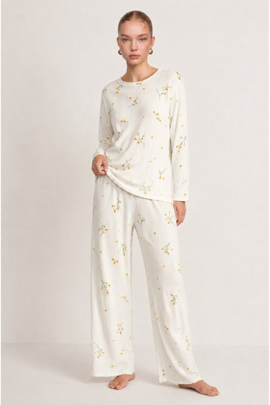 Model in een ecru pyjamaset met gele bloemen, inclusief een shirt met lange mouwen en een wijde broek.