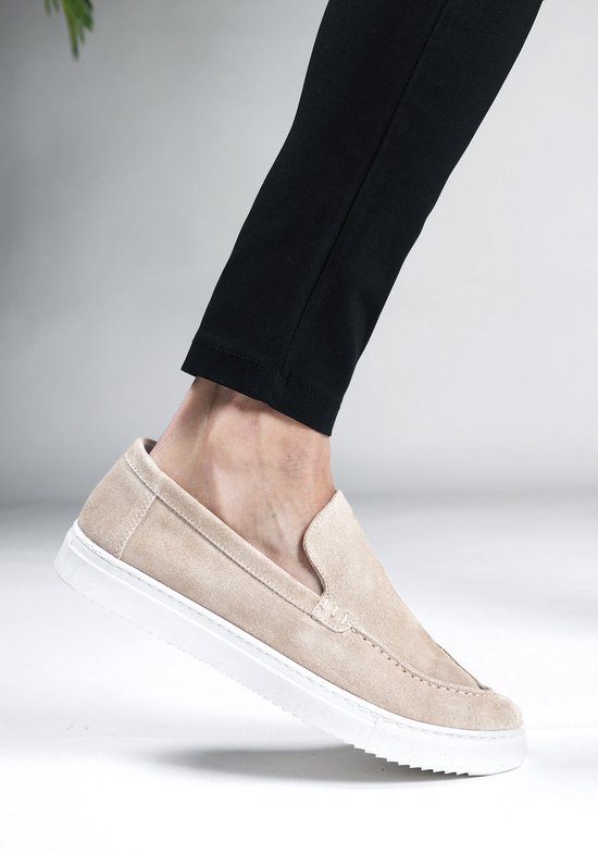 Beige suède loafer in beweging, gedragen met een zwarte broek.