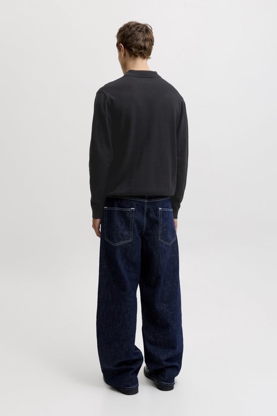 Achterkant van een model in een zwarte longsleeve poloshirt en wijde donkere jeans met witte stiksels.