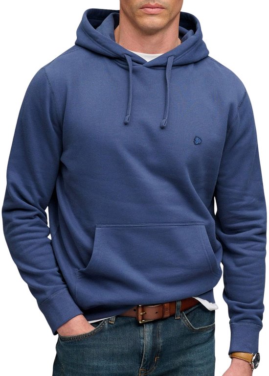 Man met sproeten in blauwe hoodie, jeans en bruine riem, handen in de zakken.