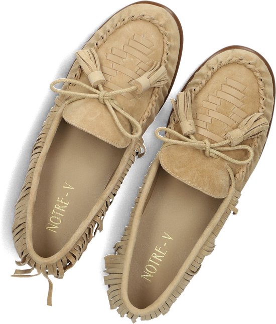 Beige suède loafers met franjes en strikdetail met kwastjes, van bovenaf gezien. Het gouden logo 'NOTRE-V' is zichtbaar in de schoen.