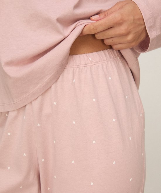 Close-up van de tailleband van een zachtroze pyjamabroek met een all-over print van kleine witte hartjes.