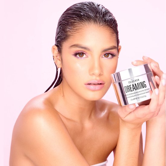 Vrouw met nat ogend haar en roze make-up houdt de zilverkleurige Color Wow Dreaming pot vast.