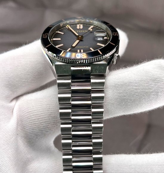 Citizen Tsuyosa horloge met zwarte wijzerplaat, gouden accenten, datumvenster en zilverkleurige stalen schakelarmband.