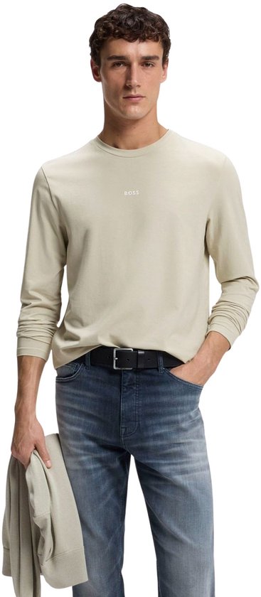Model draagt een beige T-shirt met lange mouwen en het BOSS-logo, gecombineerd met een blauwe jeans en zwarte riem.