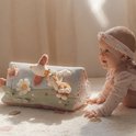 Baby kijkt lachend naar een blauwgroene speelgoed driehoek met dieren en bloemen.