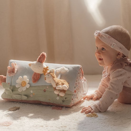 Baby kijkt lachend naar een blauwgroene speelgoed driehoek met dieren en bloemen.