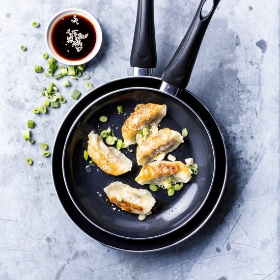 Gegrilde gyoza met lente-ui en sesamzaad in zwarte koekenpannen.