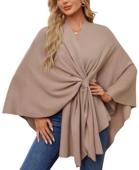 Een beige gebreide omslagdoek met een gedraaide knoop aan de voorkant, gedragen over een spijkerbroek.