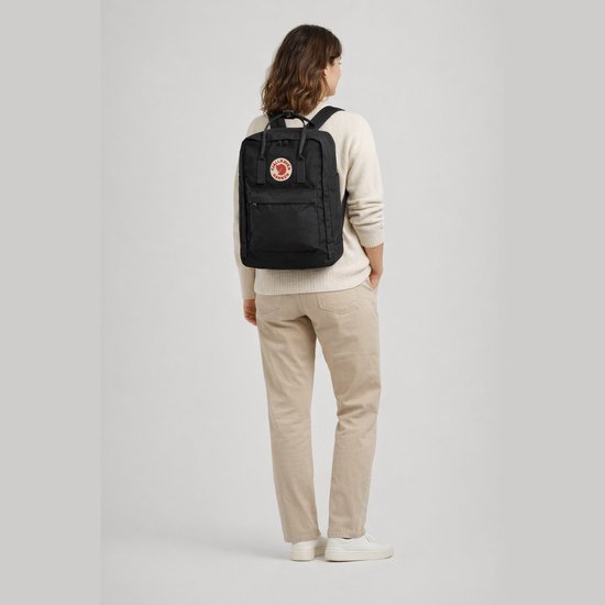 Model draagt zwarte Fjällräven Kånken rugzak met laptopcompartiment en rond logo op een crèmekleurige trui.