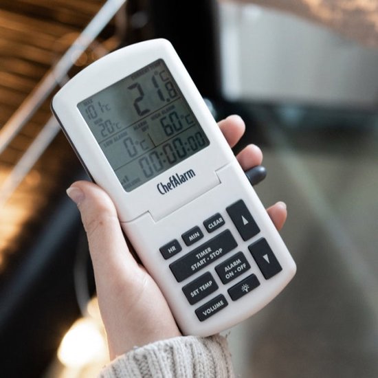 Witte ChefAlarm kookthermometer met zwart toetsenbord en LCD-scherm, vastgehouden voor een oven.