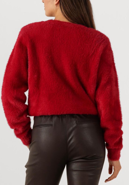 Een rode, pluizige trui met lange mouwen, gedragen door een model met haar handen in de broekzakken van een zwarte leren broek.