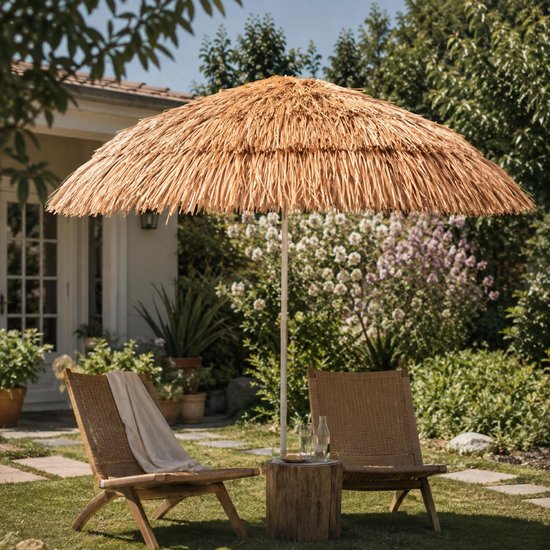 Beige raffia parasol boven twee rotan stoelen in een groene tuin.