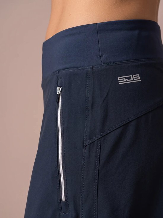 Detailopname van donkerblauwe broek met wit geritste zak en het Sjeng Sports-logo in het zilver.
