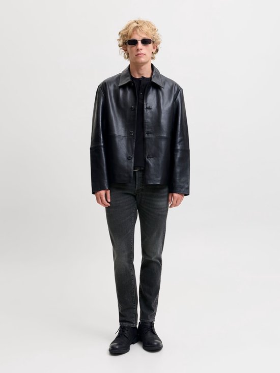Model draagt een zwarte leren jas, grijze slim fit jeans en zwarte schoenen.