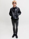 Model met blond haar en zonnebril draagt een grijze slim fit jeans en een zwarte leren jas.