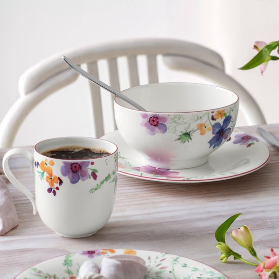 Witte porseleinen mok en kom met kleurrijke aquarelblommotieven en een subtiele rode rand op een houten tafel.