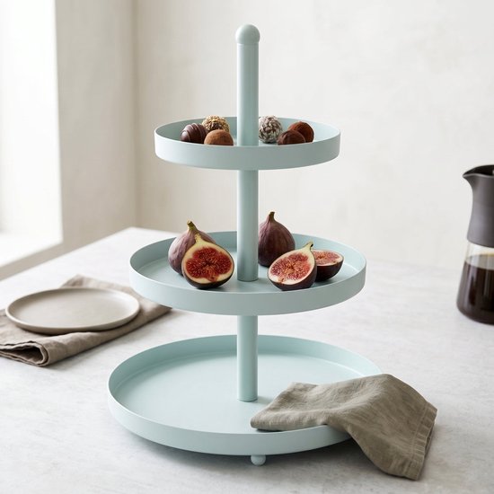 Lichtblauwe metalen etagère met drie lagen, gevuld met verschillende soorten chocolaatjes en verse vijgen.