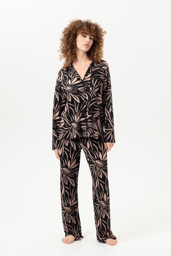 Model draagt een zwarte pyjamaset met een beige bloemenprint. Het model draagt een lange pyjamabroek en een pyjamashirt met lange mouwen en knoopsluiting.
