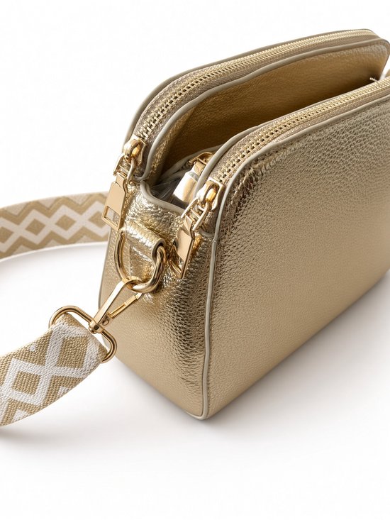 Close-up van de zijkant van een gouden crossbodytas met dubbele ritsen en goudkleurige haken.