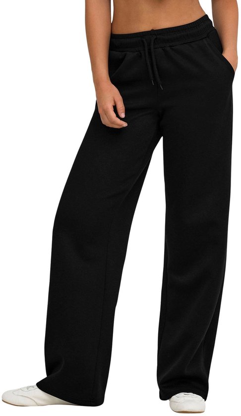 Pantalon de sport noir ample avec cordon de serrage et poches, porté par un mannequin sur des baskets blanches.