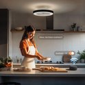 Vrouw in keuken bedient plafondventilator met stemcommando via Alexa. Ventilator op afstand bediend.