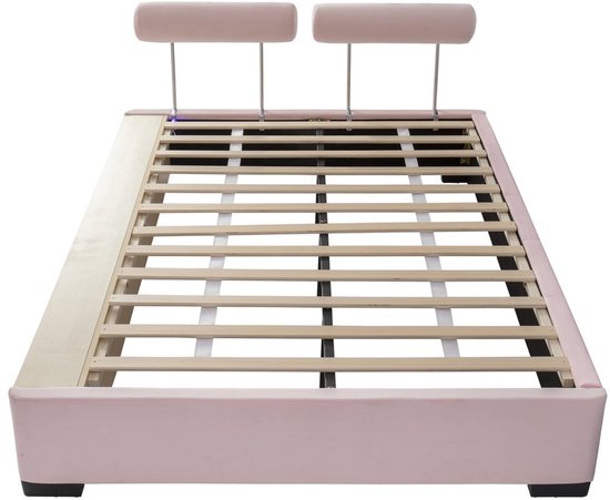 Roze bedframe zonder matras met houten lattenbodem en twee ronde, roze hoofdkussens.