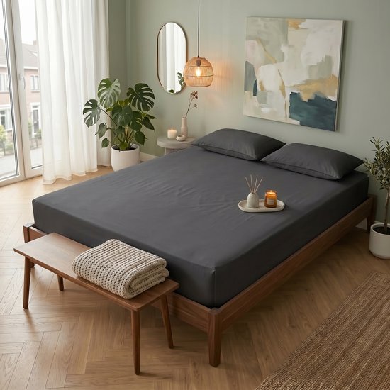 Un lit fait avec drap-housse gris foncé, oreillers et décoration dans une chambre.