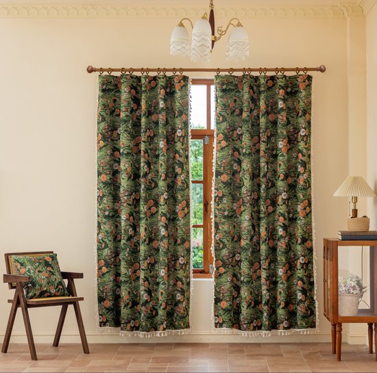 Donkergroene gordijnen met een print van oranje en witte wilde bloemen, met decoratieve witte franjes aan de zijkanten en onderkant.