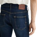 Detail van de achterkant van een donkerblauwe jeans met een bruin leren label met 'SCOTCH & SODA AMSTERDAM'.