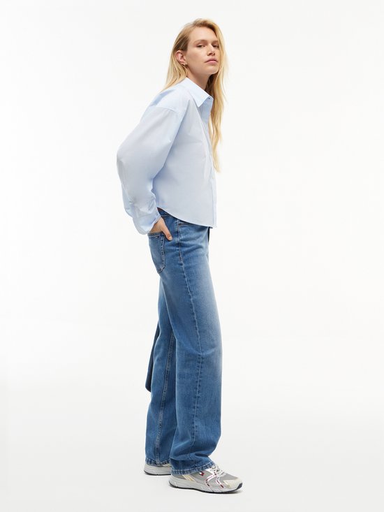 Model draagt een rechte spijkerbroek in middelblauwe wassing en een lichtblauwe blouse.