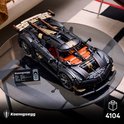 Grijze, gedetailleerde LEGO-auto met oranje interieur en gouden accenten, op een glazen tafel. "Koenigsegg" label.